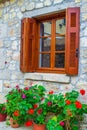 Stone house wall with wooden shutters and red flowers Greek island Royalty Free Stock Photo