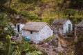 Stone houses in local style with straw covered roofs and blue windows between lush green vegetation and mountain