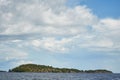 stone island overgrown with trees in the middle of the water. blue sky with clouds. northern landscape