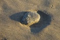 A stone lies in a hole on wet sand and casts a shadow in the rays of the evening sun, beach background Royalty Free Stock Photo