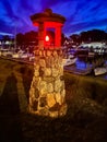 Stone lighthouse statute with red light by boats in harbor Royalty Free Stock Photo