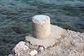 Stone mooring bollard on edge of concrete pier next to sea