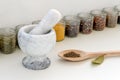 Stone mortar with pestle, large wooden spoon with ground pepper and glass jars with different spices on a white kitchen table. Royalty Free Stock Photo