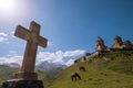 Stone Orthodox cross with a Gergeti Trinity Church with grazing horses on the green grass hill and Kazbek 5054m mountain. Wide Royalty Free Stock Photo