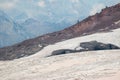 Stone outlier on red slope of Elbrus volcano with white glacier, clouds and Caucasus mountains in day time.