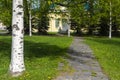 Stone-paved path to small yellow house among birches and firs