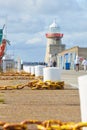 Stone pier with big white bollard and yellow metal chain for ships and white lighthouse. Royalty Free Stock Photo