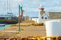 Stone pier with big white bollard and yellow metal chain for ships and white lighthouse. Royalty Free Stock Photo