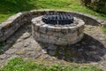 Stone round fountain with a protective grid of twisted prisms. forged steel bars go spiraled at the top. around the well there is Royalty Free Stock Photo