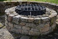 Stone round fountain with a protective grid of twisted prisms. forged steel bars go spiraled at the top. around the well there is Royalty Free Stock Photo