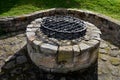 Stone round fountain with a protective grid of twisted prisms. forged steel bars go spiraled at the top. around the well there is Royalty Free Stock Photo