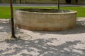 Stone round fountain with a protective grid of twisted prisms. forged steel bars go spiraled at the top. around the well there is