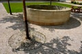 Stone round fountain with a protective grid of twisted prisms. forged steel bars go spiraled at the top. around the well there is Royalty Free Stock Photo