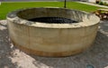 Stone round fountain with a protective grid of twisted prisms. forged steel bars go spiraled at the top. around the well there is Royalty Free Stock Photo