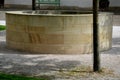 Stone round fountain with a protective grid of twisted prisms. forged steel bars go spiraled at the top. around the well there is Royalty Free Stock Photo