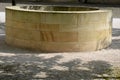 Stone round fountain with a protective grid of twisted prisms. forged steel bars go spiraled at the top. around the well there is Royalty Free Stock Photo