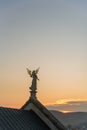 Stone sculpture of an angel with golden wings standing on the rooftop of a baroque temple at sunset. Royalty Free Stock Photo