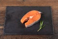 Stone serving board with portioned salmon steak and rosemary sprig over wooden background.