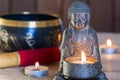 Stone sitting buddha, candles and Tibetan bowl. Around the candle, the atmosphere for meditation. Home comfort and relaxation