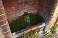 A Stone source of clear transparent water on the street. Cold water flows into a container overgrown with green moss Royalty Free Stock Photo