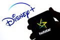 Hotstar logo on the silhouette of a smartphone hold in hand and Disney+ logo at the background. Concept. Real photo, not a montage