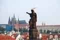 Stone statue on Charles bridge pointing to the St.Vitus Cathedral over red house roofs. Czeck Republick, Prague Royalty Free Stock Photo