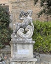 Stone statue of a cherub reclining on a seat holding a cluster of grapes in Cortona, Italy.