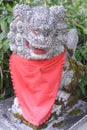 Stone statue of komainu lion-dog with a red bib in front of a shinto shrine in Japan