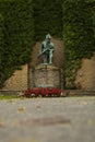 Stone statue of a soldier visible in front of a wall adorned with green foliage and plants