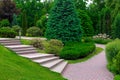 Stone steps to path from paving slabs in park on slope with ornamental plants. Royalty Free Stock Photo