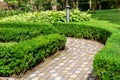 A stone tile path in a park with a hedge of evergreen deciduous shrubs.