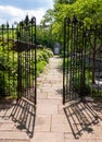 A stone walkway behind an opened wrought iron fence in a garden