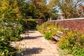 A stone walkway in a garden of flowers with two wooden benches and a brick wall in summer Royalty Free Stock Photo