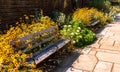 A stone walkway in a garden of flowers with two wooden benches and a brick wall in summer Royalty Free Stock Photo