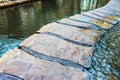 Stone walkway over water with metal strips between rocks and water splashing up on one section