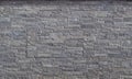 Stone wall cladding made of embossed horizontal gray stripes of rock stacked in panels