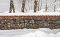 Stone wall covered by snow with trees in background Royalty Free Stock Photo