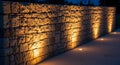 Stone wall illuminated by warm yellow spotlights at night, casting dramatic shadows and highlighting the textured Royalty Free Stock Photo