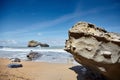 Stones on a sandy beach and a rocky island with a hole. Ocean waves. Atlantic coast in southwestern France. Summer sunny day with Royalty Free Stock Photo