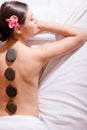 Stones therapy spa: portrait of beautiful brunette young woman having fun relaxing laying on white bed with stones and orchids Royalty Free Stock Photo