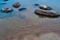 Stones with white stains on sandy shore with reflections in water of Lake Ladoga, blue shadows Royalty Free Stock Photo