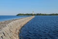 Stony breakwater dam quay and lighthouse on the Ladoga lake. Sunny summer landscape. Blue sky reflects in water surface Royalty Free Stock Photo