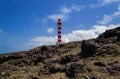 Stony landscape with white and red lighthouse and blue sky with