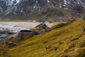 Stony meadow, snowy hillside, colorful cottage on beach Uttakleiv, Lofoten Islands