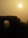 The stony ruin of medieval stronghold tower on hill. Early morning sunshine hidden in heavy mist.