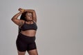 Stop body shaming. Plump, plus size african american woman in sportswear looking aside, lifting her arms up in studio