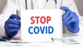 STOP COVID - text on white paper card in hands doctor