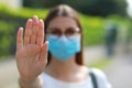 STOP COVID-19 Unidentified Woman Wearing Surgical Mask Showing STOP Gesture Looking at Camera Outdoors. Focus on open hand palm Royalty Free Stock Photo