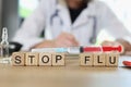 Stop flu words on wooden cubes and vaccine syringe on table, doctor in background.
