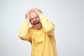 Mature man in yellow tshirt suffering from loud music and pain screaming trying to plug ears against grey background. Royalty Free Stock Photo